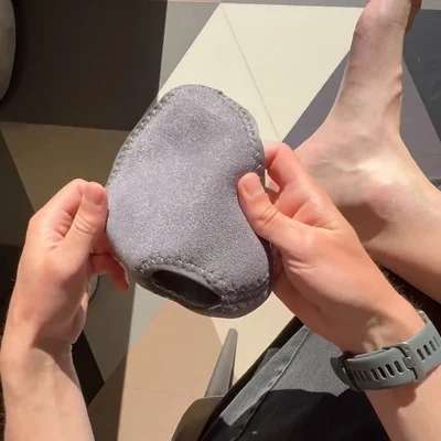 Two hands holding the open gray Stepeva wrap beside a bare foot, sneakers set behind on a diamond-pattern floor